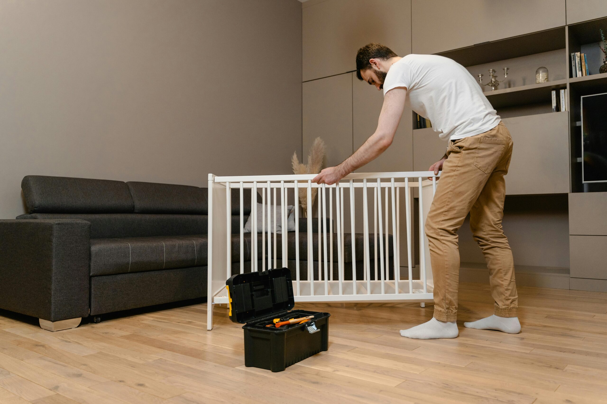 A man assembles a crib in a stylish living room with modern decor.